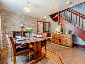Un coin repas avec une table en bois dressée pour quatre personnes, un mur en pierre et un escalier avec des rampes en bois.