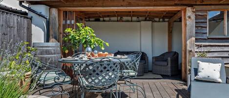 A covered outdoor patio with a table and chairs, a sofa, and a potted plant.