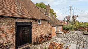 Una casa tradizionale in mattoni con una porta nera, una piccola finestra e un sentiero in pietra che conduce a un giardino con piante e una panchina in pietra.