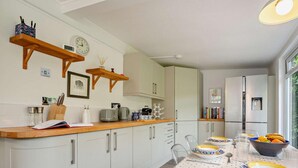A kitchen with white cabinets, wooden countertops, a clock, and a dining area with a polka dot tablecloth. - 3 Bed in Yarmouth (oc-94802) (Cranmore)