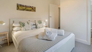 A neatly made bed with a patterned bedspread, a wall-mounted painting, and a bedside lamp. - 3 Bed in Yarmouth (oc-94802) (Cranmore)