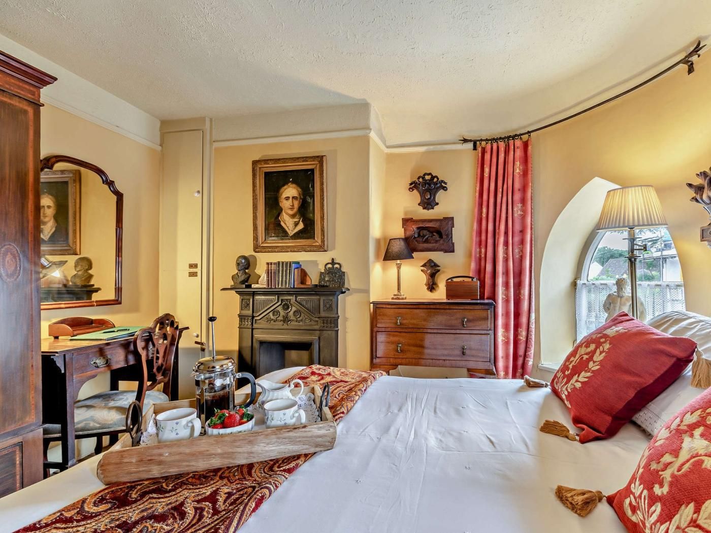 A bedroom with a bed, a desk with a chair, a fireplace, and a window with curtains.