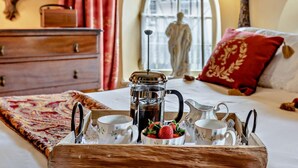 Una cama bien hecha con una bandeja de desayuno, una estatua al fondo y una ventana con cortinas.