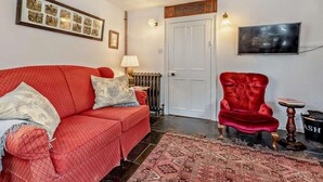 Una habitación con un sofá rojo, un sillón rojo, un tapete estampado, un radiador y un cuadro en la pared.