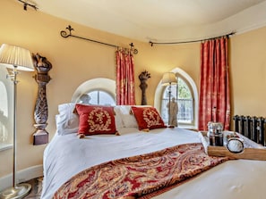 A bedroom with a large bed, two bedside lamps, a nightstand with a clock, and a window with curtains. - 1 Bed in Bridgwater (oc-95168) (Nether Stowey)