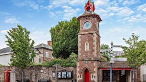 Una torre histórica con un reloj, una puerta roja y un cartel con indicaciones.