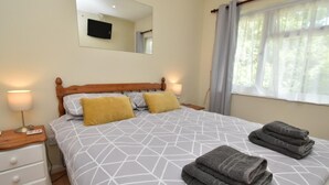 A bedroom with a bed, two bedside lamps, a nightstand, a mirror, and a window with curtains. - 2 Bed in Tenby (oc-fb196) (Tenby)