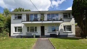 A two-story residential building with a front porch, a pathway leading to the entrance, and a small garden area. - 2 Bed in Tenby (oc-fb196) (Tenby)