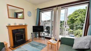 A living room with a fireplace, a television, a sofa, and a view of the outdoors. - 2 Bed in Tenby (oc-fb196) (Tenby)