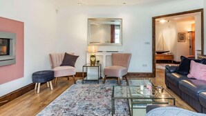 Ein Wohnzimmer mit Kamin, zwei Sesseln, einer Couch, einem Couchtisch und einem Spiegel.