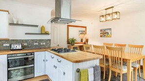 Eine Küche mit Herd, Backofen und einer Essecke mit Holztischen und -stühlen.