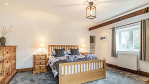 Ein Schlafzimmer mit einem hölzernen Bett, Nachttischen, einem Heizkörper, einem Fenster mit Vorhängen und einer Deckenleuchte.
