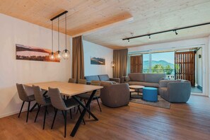 Un salon moderne avec un plafond en bois, une table à manger avec des chaises, un canapé et une grande fenêtre offrant une vue sur les montagnes.