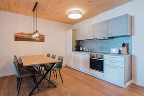 A modern kitchen with white cabinets, a wooden dining table, and a hanging light fixture. - Apartement with lake view (Unterburg am Klopeiner See)
