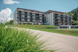 A modern multi-story hotel with balconies, a flat roof, and a landscaped area in front. - Apartement with lake view (Unterburg am Klopeiner See)