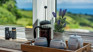 Ein Holztablett mit einer French-Press-Kaffeemaschine, zwei Tassen und einem Teekessel auf einem Fensterbrett.