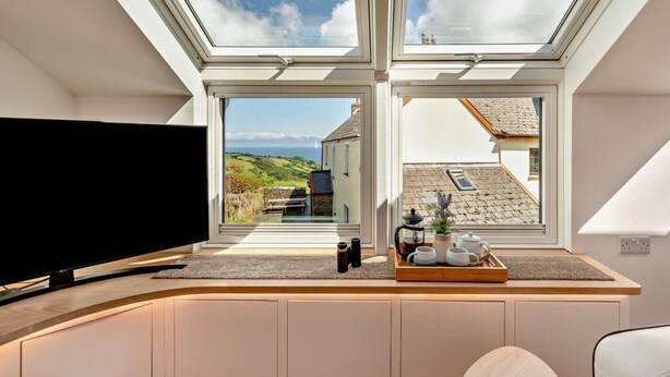 Ein Zimmer mit einem großen Fernseher, einem Tablett mit Tassen und einem Teekessel sowie Blick auf ein Haus und Hügel.
