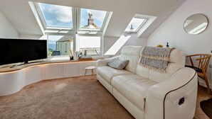 Ein modernes Schlafzimmer im Loft-Stil mit Dachfenstern, einem großen Fenster, einem Flachbildfernseher, einem weißen Ledersofa und einem kleinen Beistelltisch.