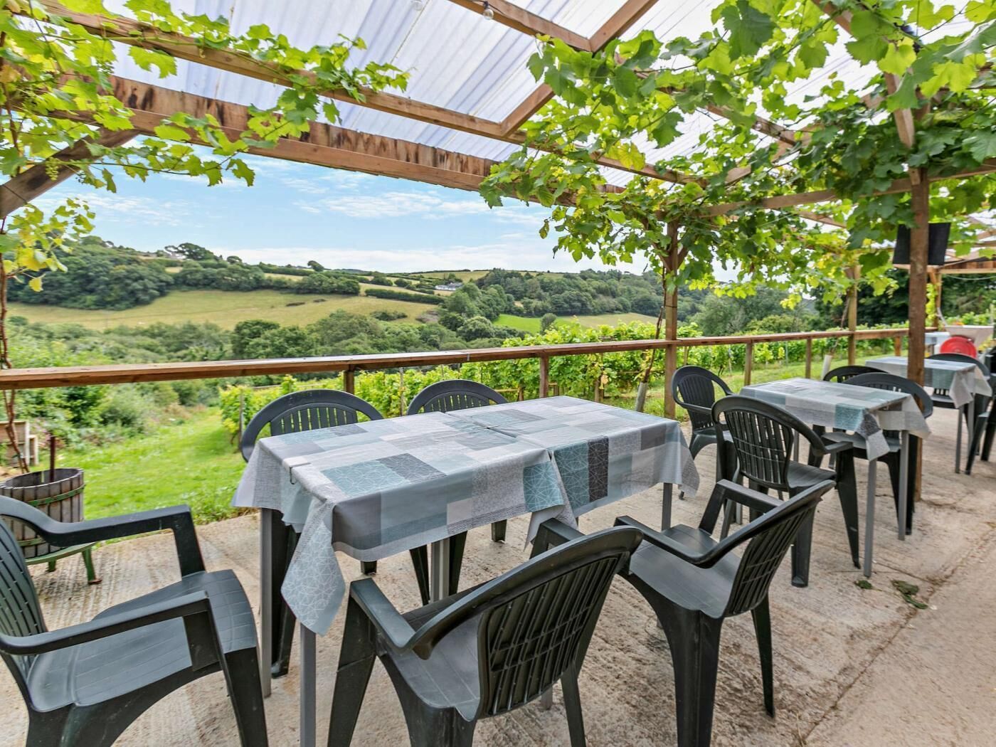 Ein Außenbereich mit Tischen und Stühlen, einer Pergola und Blick auf eine grüne Landschaft.