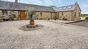 A stone building with a gravel courtyard, a potted tree, and a wooden door. - 1 Bed in Glasgow (oc-83392) (Eaglesham)