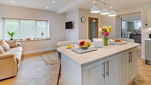 Una cocina moderna con una isla central, un comedor con un sofá y una sala de estar con ventanal.