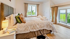 Un dormitorio con una cama grande, una lámpara de noche, un ventanal con cortinas y vistas al exterior.