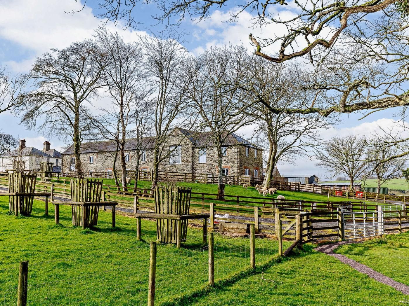 A stone building with a grassy field in front, wooden fences, and a clear sky.