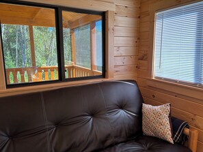 Interior de cabana de madeira com sofá de couro e janela com vista para um deck.