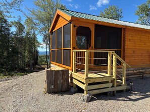 A wooden cabin with a porch and large windows, surrounded by trees and gravel ground. - Cozy 1-bedroom log cabin in peaceful Gouldsboro with AC & view of Frenchman Bay (Gouldsboro)