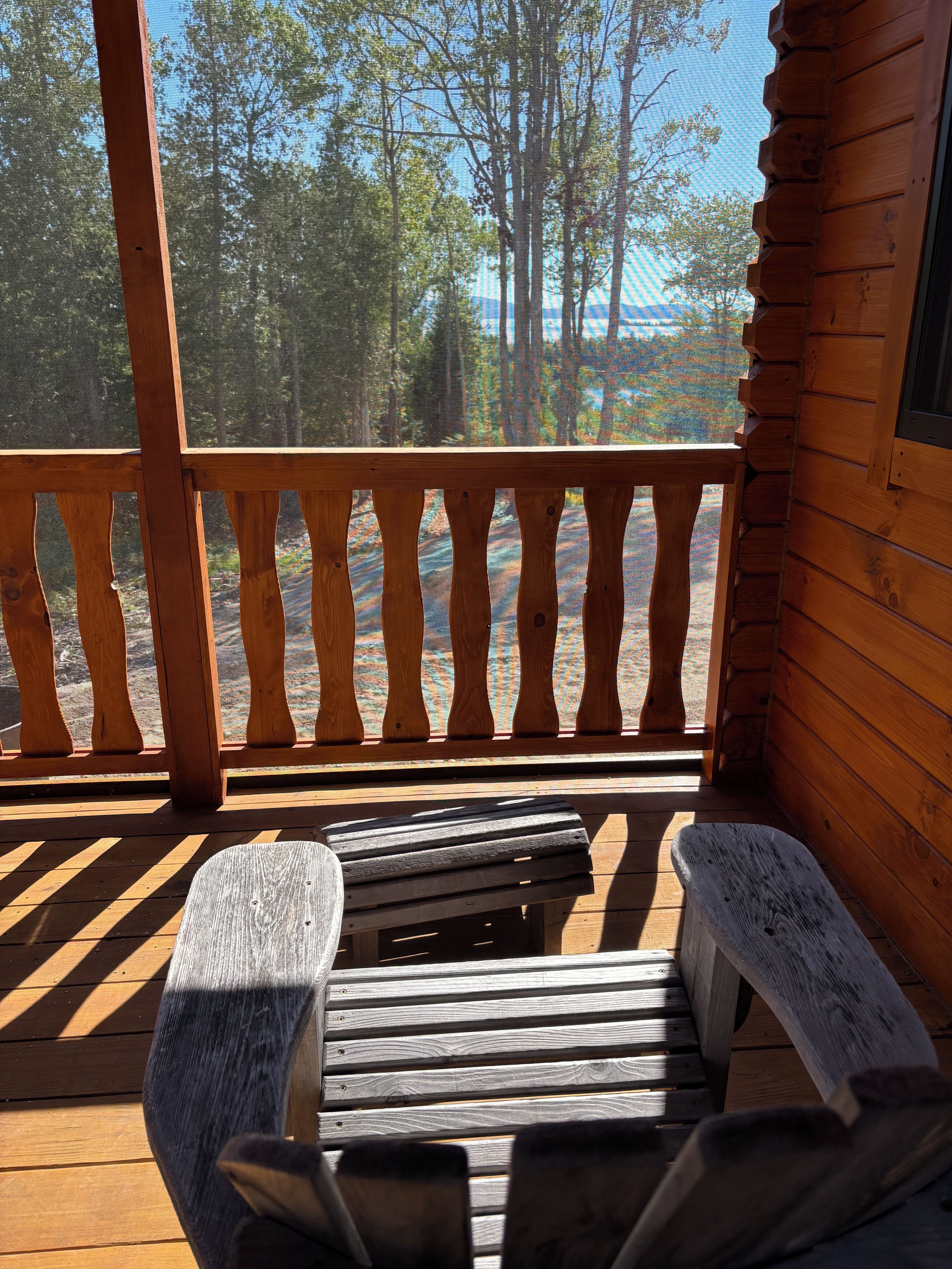 A wooden deck with a bench and a table, overlooking a forested area.