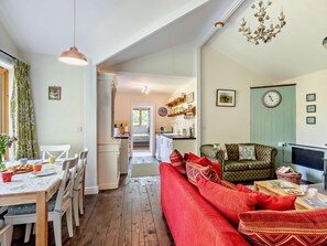 A cozy living room with a red sofa, a dining area with a table and chairs, and a kitchen visible through an open doorway.