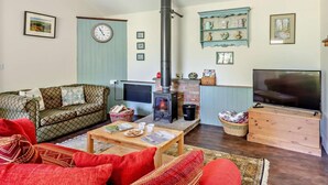 A cozy living room with a fireplace, a sofa, a television, and a clock on the wall. - 3 Bed in Watchet (oc-95161) (Washford)
