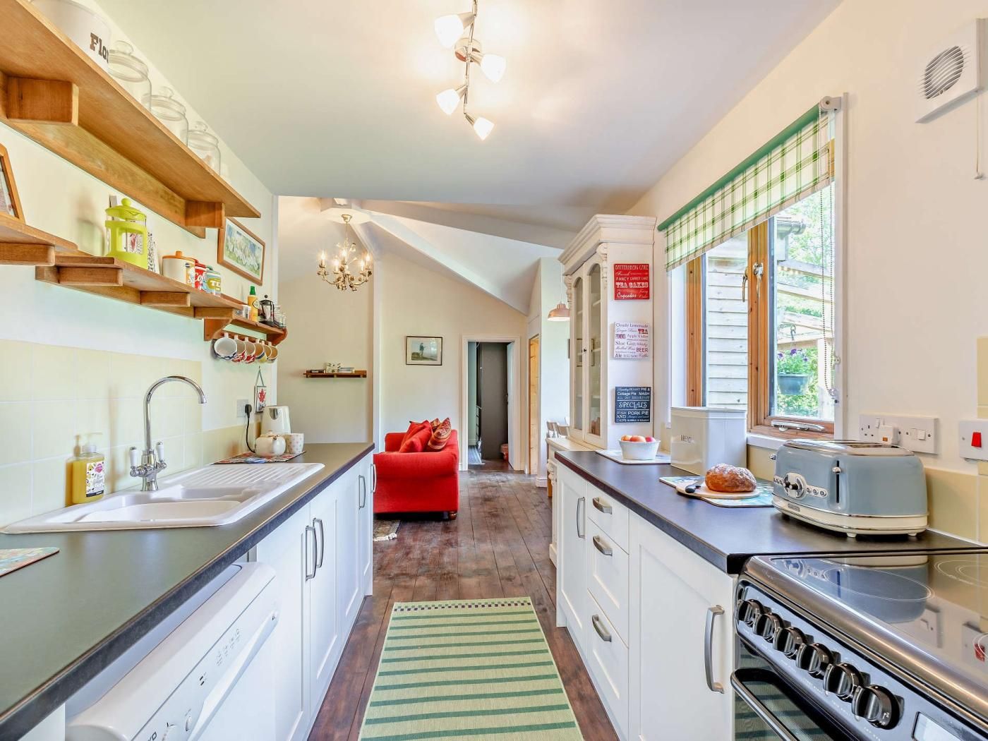 A kitchen with a stove, sink, and a red sofa in the background.