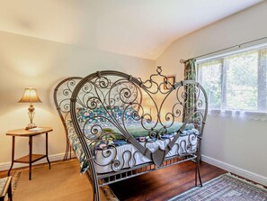 A room with a metal bed frame, a small table with a lamp, and a window with curtains.