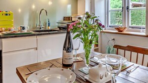 Una cucina con un tavolo da pranzo apparecchiato per due persone, una bottiglia di vino e un vaso con fiori.