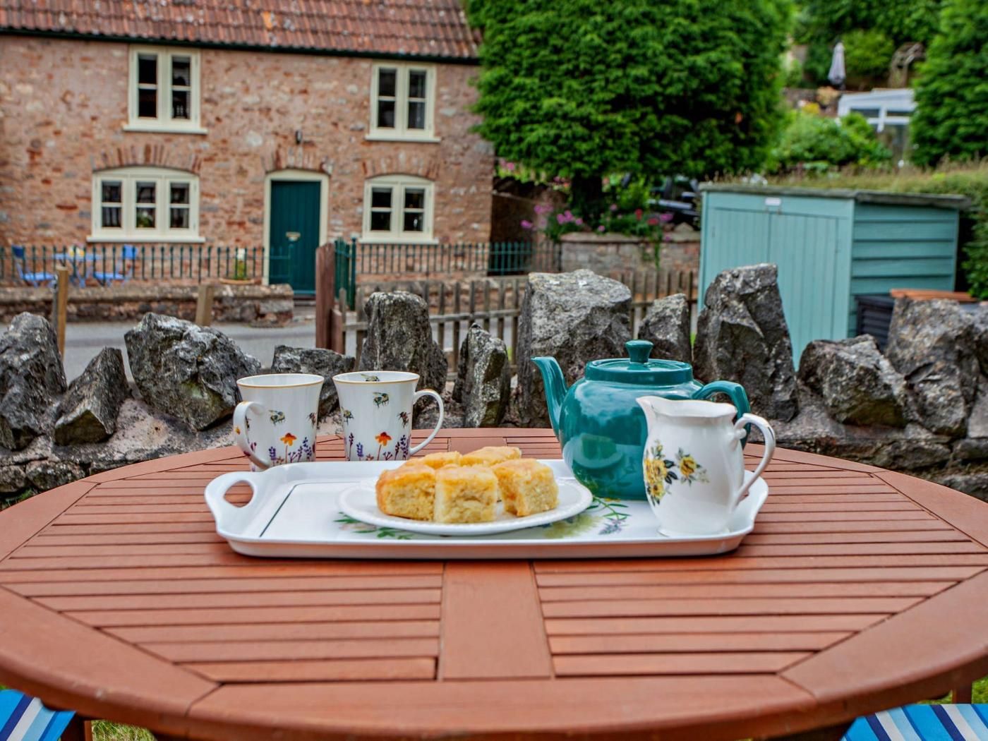 A round wooden table with a tray holding a teapot, cups, and biscuits.