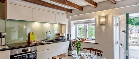 A kitchen with a Bosch oven, a dining table set for four, wooden beams on the ceiling, and a window with a view of greenery.