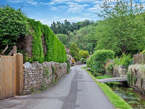 A narrow road flanked by stone walls and lush greenery, leading to a quaint village with traditional houses. - 1 Bed in Bristol (oc-95178) (Blagdon)
