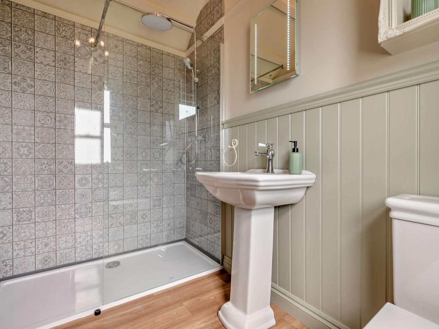 A bathroom with a shower, a pedestal sink, and a toilet.