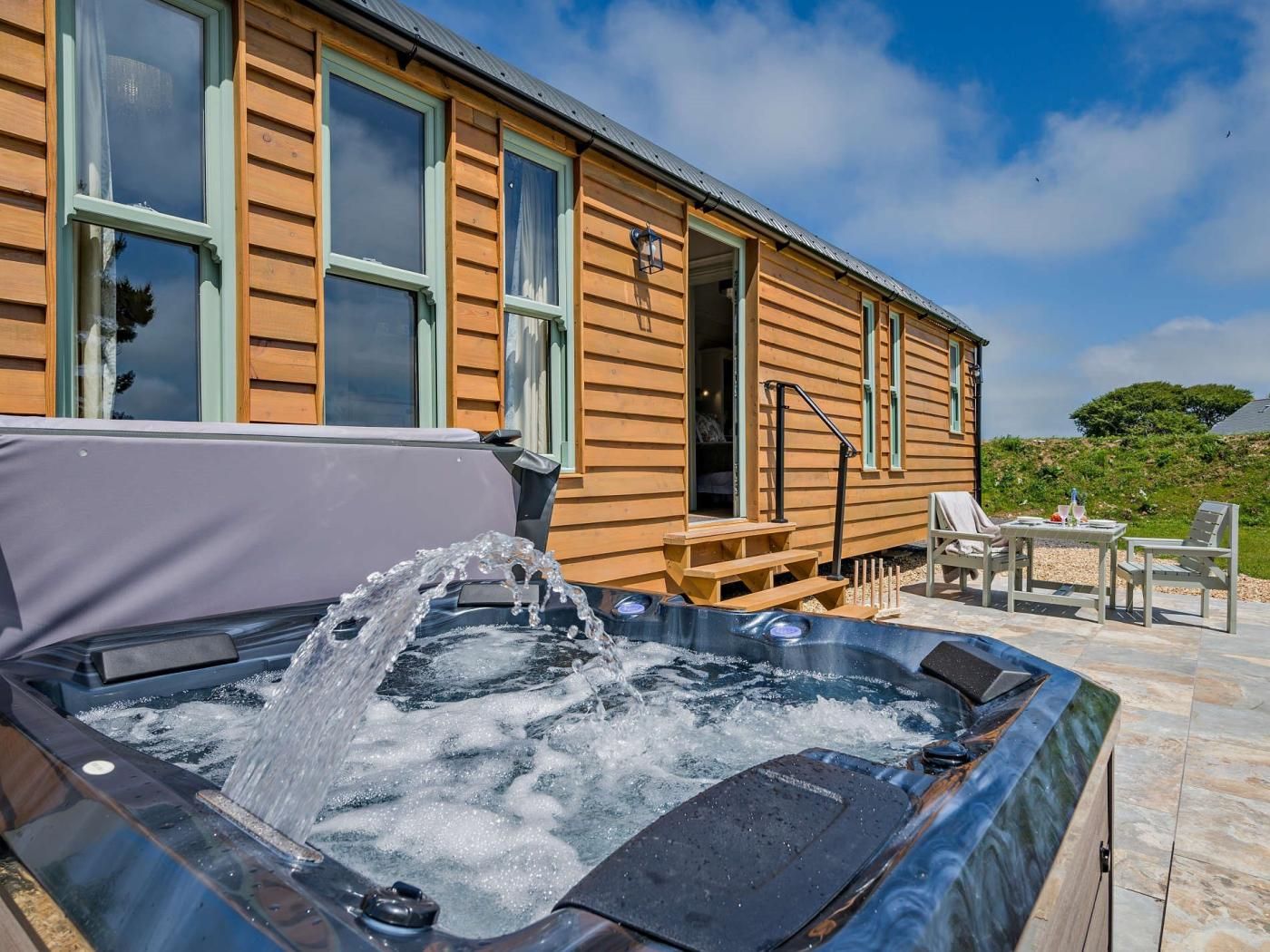 A wooden cabin with a hot tub, outdoor seating, and a clear sky.