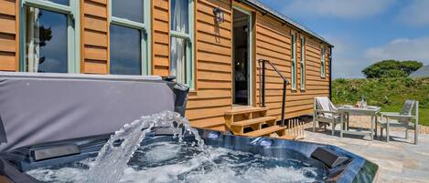 A wooden cabin with a hot tub, outdoor seating, and a clear sky.