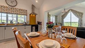 A dining area with a wooden table set for four, a clock on the wall, and a view of the outdoors. - 2 Bed in Llanarth (oc-95322) (Llanarth)