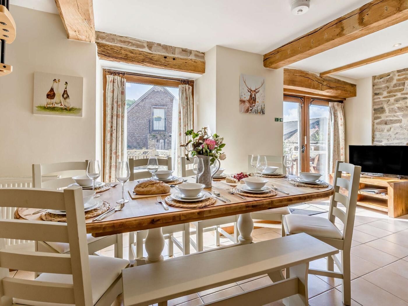A dining area with a wooden table set for four, white chairs, and a stone wall.