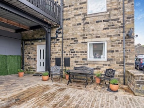 A stone building with a wooden balcony, a door, and a window. There is a table and chairs outside. - 2 Bed in Holmfirth (oc-95230) (Holmfirth)