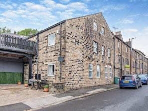A stone building with multiple windows and a paved area with benches and potted plants. - 2 Bed in Holmfirth (oc-95230) (Holmfirth)