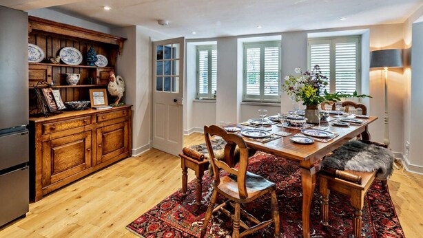 A dining area with a wooden table set for four, surrounded by chairs, a patterned rug, and a kitchen area with wooden cabinetry and a refrigerator. - 3 Bed in Kelso (oc-95231) (Kelso)