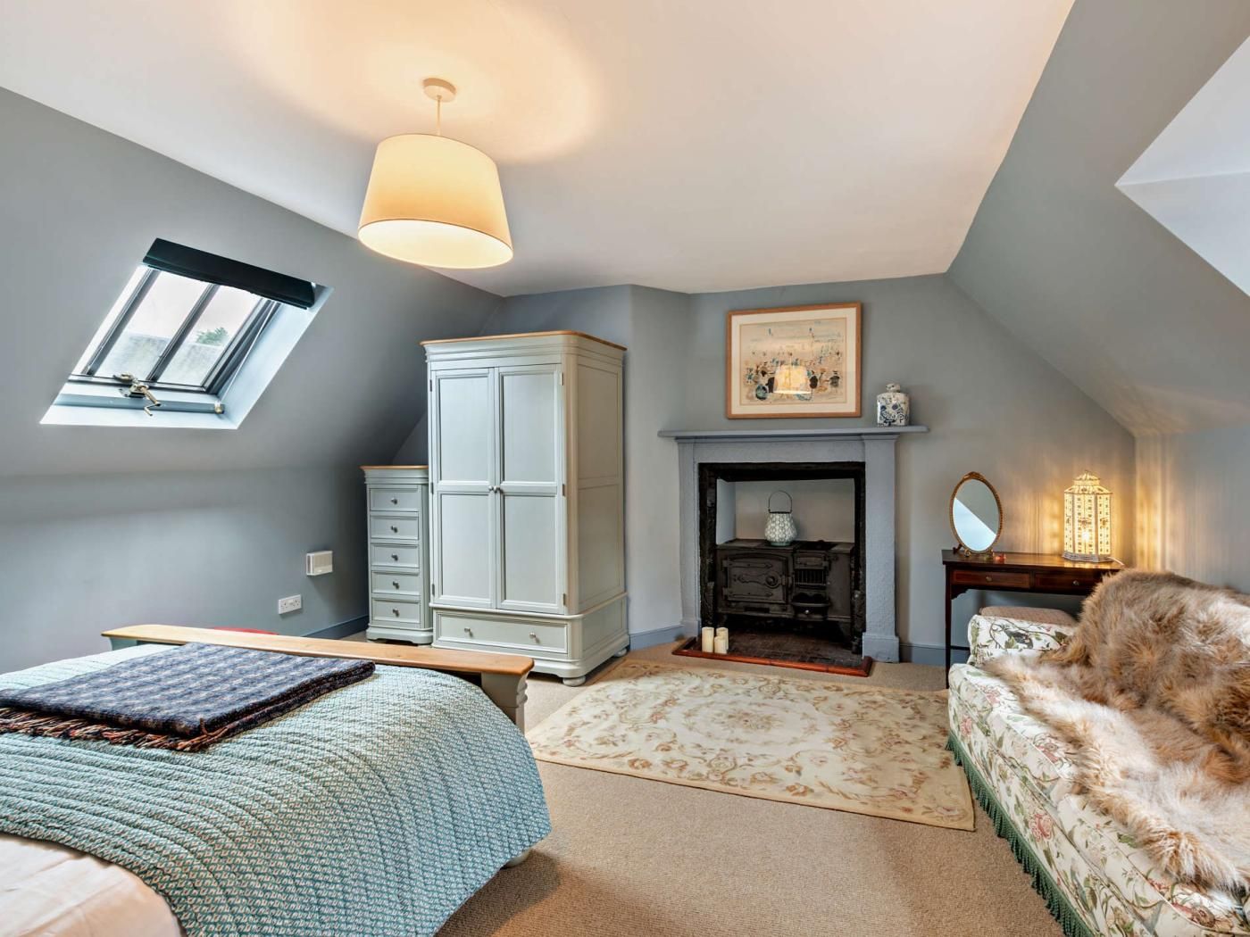 A bedroom with a bed, a dresser, a fireplace, and a window.