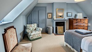A bedroom with a sloped ceiling, a fireplace, a wooden dresser, a floral armchair, and a bed with a blue blanket. - 3 Bed in Kelso (oc-95231) (Kelso)