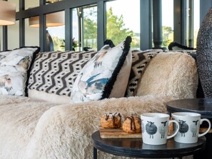 A cozy seating area with a sofa, fluffy cushions, and a small table with pastries and mugs.