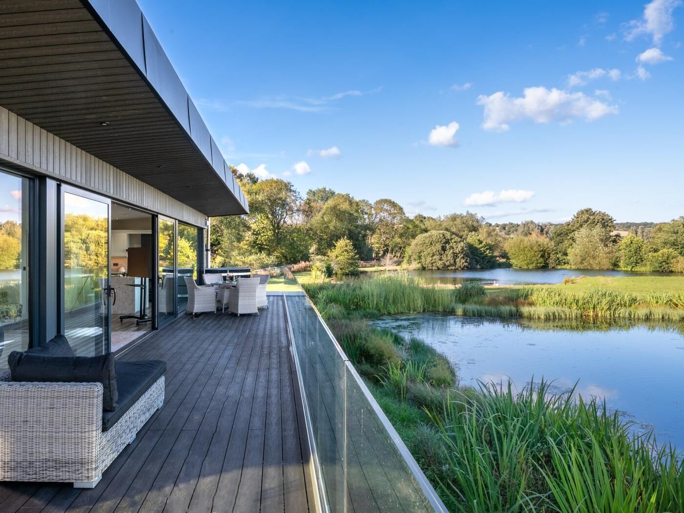 A modern house with a deck overlooking a lake, surrounded by greenery.